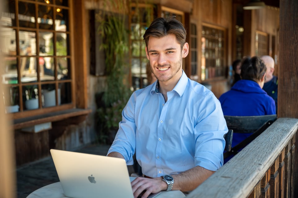 Alexander Mussler sitting in front of his computer at a cafe, smiling